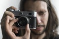 Handsome young bearded man with a long hair and in a black shirt holding vintage old-fashioned film camera on a white Royalty Free Stock Photo