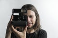 Handsome young bearded man with a long hair and in a black shirt holding vintage old-fashioned film camera on a white Royalty Free Stock Photo