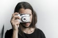 Handsome young bearded man with a long hair and in a black shirt holding vintage old-fashioned film camera on a white Royalty Free Stock Photo