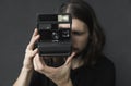 Handsome young bearded man with a long hair and in a black shirt holding vintage old-fashioned film camera on a black Royalty Free Stock Photo