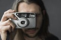 Handsome young bearded man with a long hair and in a black shirt holding vintage old-fashioned film camera on a black Royalty Free Stock Photo