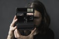 Handsome young bearded man with a long hair and in a black shirt holding vintage old-fashioned film camera on a black Royalty Free Stock Photo