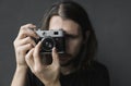 Handsome young bearded man with a long hair and in a black shirt holding vintage old-fashioned film camera on a black Royalty Free Stock Photo