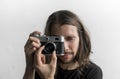 Handsome young bearded man with a long hair and in a black shirt holding vintage old-fashioned film camera on a white Royalty Free Stock Photo