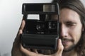 Handsome young bearded man with a long hair and in a black shirt holding vintage old-fashioned film camera on a white Royalty Free Stock Photo