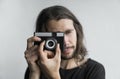 Handsome young bearded man with a long hair and in a black shirt holding vintage old-fashioned film camera on a white Royalty Free Stock Photo