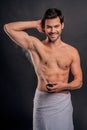 Handsome young bearded man . Shirtless muscular man is standing on gray background and using deodorant. Men care concept Royalty Free Stock Photo