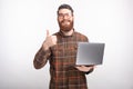 Handsome young bearded man is showing thumb up or like gesture while he is holding his laptop on white background Royalty Free Stock Photo