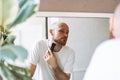 Handsome young bearded man trimming his beard with machine in bathroom at home Royalty Free Stock Photo