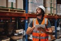 Handsome young bearded man wearing safety vest and hard hat using digital tablet entering data in warehouse standing Royalty Free Stock Photo