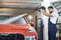 Handsome young bearded man worker washing modern red luxury car under high pressure Royalty Free Stock Photo