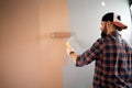 handsome young bearded painter in baseball cap and plaid shirt painting wall with paint roller. Man painting house in Royalty Free Stock Photo