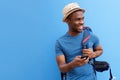 Handsome young black man with bag and mobile phone smiling against blue background Royalty Free Stock Photo