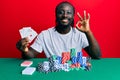Handsome young black man playing poker holding cards doing ok sign with fingers, smiling friendly gesturing excellent symbol Royalty Free Stock Photo