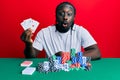 Handsome young black man playing poker holding cards scared and amazed with open mouth for surprise, disbelief face Royalty Free Stock Photo