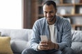 Handsome Young Black Man Using Smartphone While Relaxing On Couch At Home Royalty Free Stock Photo