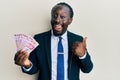 Handsome young black man wearing business suit holding mexican pesos banknotes pointing thumb up to the side smiling happy with Royalty Free Stock Photo