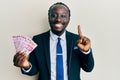 Handsome young black man wearing business suit holding mexican pesos banknotes smiling with an idea or question pointing finger Royalty Free Stock Photo