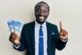 Handsome young black man wearing business suit holding 100 rands banknotes smiling with an idea or question pointing finger with Royalty Free Stock Photo