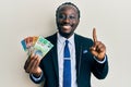 Handsome young black man wearing business suit and tie holding australian dollars smiling with an idea or question pointing finger Royalty Free Stock Photo