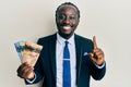 Handsome young black man wearing business suit and tie holding canadian dollars smiling with an idea or question pointing finger Royalty Free Stock Photo