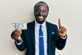 Handsome young black man wearing business suit and tie holding 100 dollars smiling with an idea or question pointing finger with Royalty Free Stock Photo