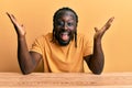 Handsome young black man wearing casual clothes sitting on the table celebrating crazy and amazed for success with arms raised and Royalty Free Stock Photo