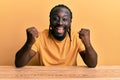 Handsome young black man wearing casual clothes sitting on the table celebrating surprised and amazed for success with arms raised Royalty Free Stock Photo