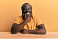 Handsome young black man wearing casual clothes sitting on the table looking confident at the camera smiling with crossed arms and Royalty Free Stock Photo