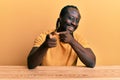 Handsome young black man wearing casual clothes sitting on the table pointing fingers to camera with happy and funny face Royalty Free Stock Photo