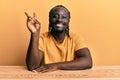 Handsome young black man wearing casual clothes sitting on the table smiling with happy face winking at the camera doing victory Royalty Free Stock Photo