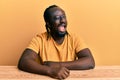 Handsome young black man wearing casual clothes sitting on the table winking looking at the camera with sexy expression, cheerful Royalty Free Stock Photo