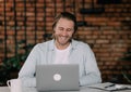 handsome young blond man sits at his desk with a laptop and smiles. successful it-specialist or freelancer Royalty Free Stock Photo