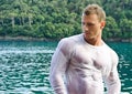 Handsome young bodybuilder by the sea with wet shirt on