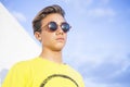Handsome young boy man with blonde hair and black sunglasses stand and pose with yellow shirt and blue sky background - caucasian