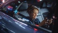 Handsome Young Boy is Sitting on Backseat of a Car, Commuting Home at Night. Passenger Playing Video