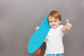 Handsome young boy wearing a casual outfit, hold his skateboard on his shoulder, raising his thumb up, standing on a Royalty Free Stock Photo