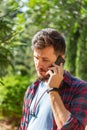 Handsome young brunette man tilted his head and speaks on the phone. Portrait of a man with a beard and mustache on a natural