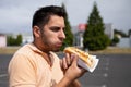 Handsome brunette man eating hot dog in the parking lot .