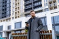 A handsome young business man in fashion coat at office building background. Male is using phone. Closeup. Front view. Royalty Free Stock Photo