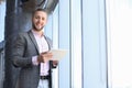 Handsome young business man holding digital tablet and looking at camera with smile while standing in the office Royalty Free Stock Photo