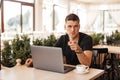 Handsome young business man is sitting in a cafe with a laptop with coffee and is pointing his finger at you. Successful Royalty Free Stock Photo