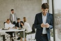 Handsome young business man standing confident in the office and suing mobile phone Royalty Free Stock Photo