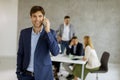 Handsome young business man standing confident in the office and suing mobile phone Royalty Free Stock Photo