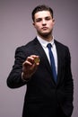 Handsome young business man in suit with bitcoin in hand pointed on camera isolated on gray background