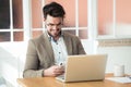 Handsome young business man using his smartphone while working with laptop in the office Royalty Free Stock Photo