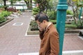 Handsome young business man using mobile phone while leaning a green pole at outdoor park. Royalty Free Stock Photo