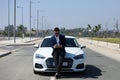 Handsome young businessman with beard and blue suit standing next to his white sports car. The man is wearing sunglasses and Royalty Free Stock Photo