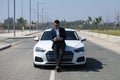 Handsome young businessman with beard and blue suit standing next to his white sports car. The man is wearing sunglasses and Royalty Free Stock Photo