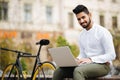 Handsome young indian businessman dressed in suit working on laptop computer while sitting outdoors near bicycle Royalty Free Stock Photo